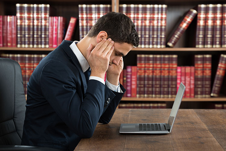 Man at desk with his eyes closed rubbing his temples in front of his laptop